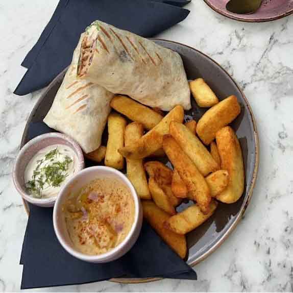 Ada’s Cafe & Bistro two chicken wraps, a side of potato wedges, and a bowl of dipping sauce.